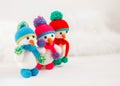 Three Little cute crocheted snowmans in a multicolor hats and scarfs on a white wooden background