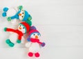 Three Little cute crocheted snowmans in a multicolor hats and scarfs on a white wooden background