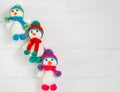 Three Little cute crocheted snowmans in a multicolor hats and scarfs on a white wooden background