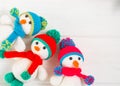 Three Little cute crocheted snowmans in a multicolor hats and scarfs on a white wooden background