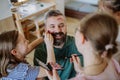 Three little girls putting on make up on their father, fathers day with daughters at home.