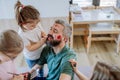 Three little girls putting on make up on their father, fathers day with daughters at home.