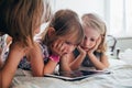 Three little sisters indoor at home using tablet lying in bed Royalty Free Stock Photo