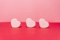 Three little white hearts situating on a line in front of the camera. Behind them there are a pink background. San Valentine`s da
