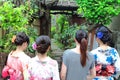 Three local Japanese young women wearing typical clothes and an European tourist walk together through a Japanese typical garden.