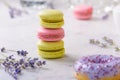 Three macarons and sprigs lavender in the center of the image, one lilac donut in front, one pink macaron behind, on white marble