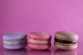 Three macaroons lilac brown chocolate lavender pink lie in a row on a pink fuchsia-colored background with reflection and a place