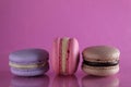 Three macaroons lilac brown chocolate lavender pink lie in a row on a pink fuchsia-colored background with reflection and a place