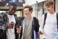 Three Male College Students Reading Text Message On Mobile Phone