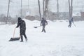 Three male workers remove snow with shovels and scrapers. It is snowing heavily outside. The snowfall.