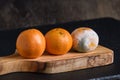 Three mandarin oranges on a black cutting board, one fresh, one going bad, and one very moldy