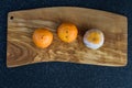 Three mandarin oranges on a wooden cutting board, one fresh, one going bad, and one very moldy