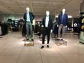 Three mannequins of men dressed in casual clothes are standing in the hall with showcases and shelves of a clothing store