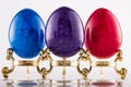 Three marble textured stone easter eggs on gold stands for eastern holiday in purple, blue and red.