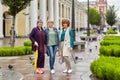 Three mature women stand on a city street in rainy weather and look at the camera.
