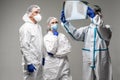 Three medical healthcare workers exam x-ray at meeting in biohazard protective tools standing isolated on gray background. Ready Royalty Free Stock Photo