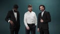 Three men friends in tuxedos are posing, smiling and looking at the camera funny