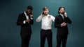 Three men friends in tuxedos are standing together and talking to the phones in slow motion