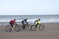Three men on mountain bike on beach with blue sky