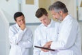 Three men in white coats looking at clipboard