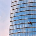 Three men workers in red and dark work clothes cleaning the exterior windows of a business skyscraper, bottom view