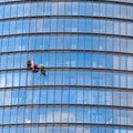 Three men workers in red and dark work clothes cleaning the exterior windows of a business skyscraper