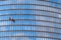 Three men workers in red and dark work clothes cleaning the exterior windows of a business skyscraper