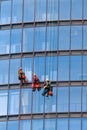 Three men workers in red and dark work clothes cleaning the exterior windows of a business skyscraper. Outdoor