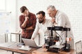 Three men are working on preparing a 3d printer for printing. One of them explains the rest of the subtlety the print.