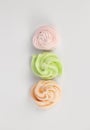 Three meringues pink green orange on a white background. View from above