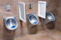 Three metal urinals with automatic water flush sensor after urinate, Men`s toilet trimmed with brown marble tiles