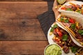 Three Mexican tacos with marbled beef, black Angus and vegetables on old rustic table. Mexican dish with sauces guacamole and sals Royalty Free Stock Photo