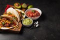 Three Mexican tacos with marbled beef, black Angus and vegetables on wooden Board on a dark stone background. Mexican dish with sa