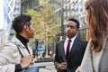 Three millennial business colleagues standing on the street talking, low angle, close up