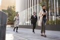 Three millennial city workers walking in the street, low angle, full length