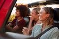 Three millennial female friends on a road trip driving together in an open jeep, close up