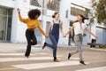 Three millennial hip girlfriends holding hands and laughing as they run across a pedestrian crossing Royalty Free Stock Photo