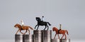 Three miniature men riding horses on piles of coins. Three pile of coins in the shape of a podium.