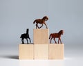 Three miniature racehorses standing on a block of trees shaped like a podium.