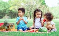 Three mixed race caucasian little cute children kids sitting, playing in outdoor green park for picnic, eating fruit, watermelon Royalty Free Stock Photo