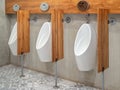 Three modern white automatic urinal for men and wood partitions on cement wall in toilet