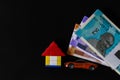 Three money notes bundles, a lego house and one toy car on black background with copy space