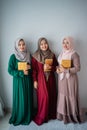 Three moslem women smilling hold the holy book of Al-Quran