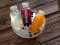 Three multi-colored bottles with fruit drink in a cup with ice on a board.