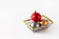 Three multi-colored Christmas balls are in a shopping basket on a white background. The concept of Christmas and New Year shopping Royalty Free Stock Photo