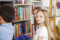 Three multiethnic children look for books near bookshelves and read together in school library