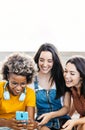 Three multiracial women friends using mobile phone sitting outdoors Royalty Free Stock Photo