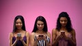 Three multiracial women scrolling smartphone on pink background, place for text