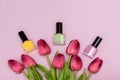 Three nail polish bottles: green, yellow and pink with fresh spring tulip flowers on a pink background