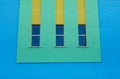 Three narrow vertical windows of green and yellow colors on the blue brick wall Royalty Free Stock Photo